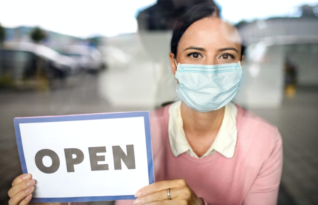 Portrait of teacher with face mask after lockdown, holding open sign