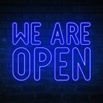 We are open - blue neon light word on brick wall background